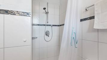 Une douche équipée d’un pommeau de douche et d’un flexible de douche, d’un porte-serviettes et d’un rideau de douche orné de motifs en forme de lettres.
