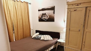 Um quarto com cama, cadeira, guarda-roupa e um quadro na parede.