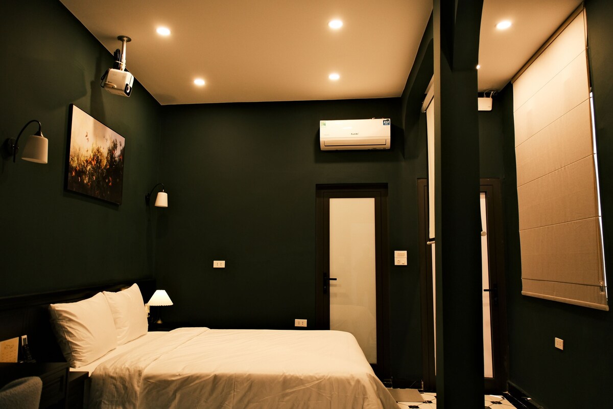 Una habitación de hotel con cama, lámparas de noche, aire acondicionado y una puerta.