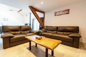 Un salon avec deux canapés en cuir marron, une table basse en bois et un panneau mural portant l’inscription « LONDRES ».