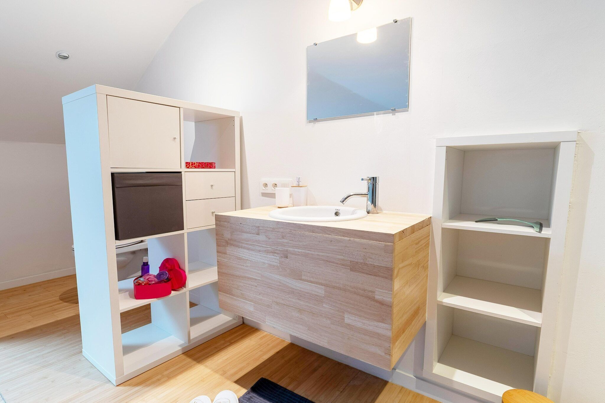 A modern bathroom with a wooden vanity, a mirror, and a built-in shelf.