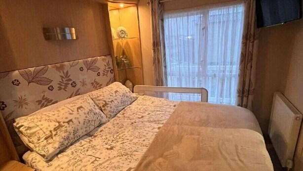Ein Hotelzimmer mit Bett, Sessel, Nachttisch, Heizkörper und Fenster mit Vorhängen.