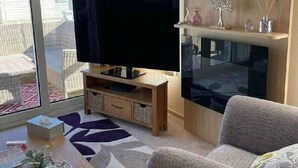 Ein modernes Wohnzimmer mit Flachbildfernseher, einer Couch, einem Couchtisch und einem großen Fenster mit Blick auf Gebäude.