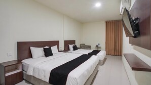 Une chambre d’hôtel avec deux lits, un téléviseur fixé au mur, une petite table et un rideau.