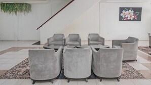 Un intérieur moderne avec des chaises grises à revêtement en tissu disposées autour d’une table centrale, un escalier et une plante fixée au mur.