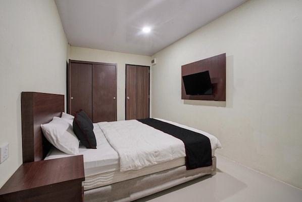 Une chambre à coucher avec un lit, une armoire en bois et un téléviseur fixé au mur.