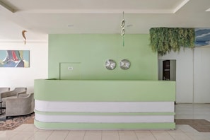 Un comptoir d’accueil aux couleurs vert et blanc, deux horloges murales et une plante suspendue.