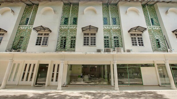 A building with a symmetrical facade, large windows with green lattice designs, and a central entrance with glass doors.