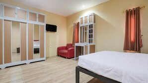 A bedroom with a bed, a red chair, a wardrobe, and a mirror.