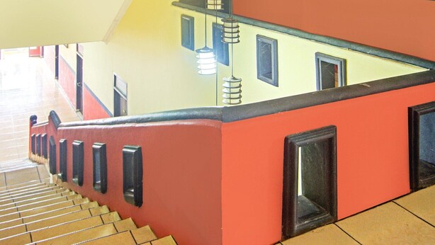 A staircase with a red and yellow wall, black railings, and a light fixture. - Cozy Twin Escape in Indonesia with Free WiFi (Bandar Lampung)
