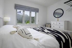 A bedroom with a large bed, a window with a view, a dresser, and a mirror. - Hampton Coast (Abersoch)