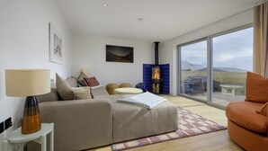 Een moderne woonkamer met een bank, een tafel, een lamp, een open haard en een groot raam.