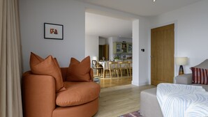 Een woonkamer met een bank, een bijzettafeltje en een lamp. Er is een deur die naar een andere kamer leidt.