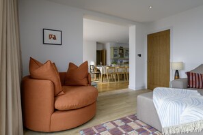 A living room with a sofa, a coffee table, and a lamp. There is a door leading to another room. - Hampton Coast (Abersoch)