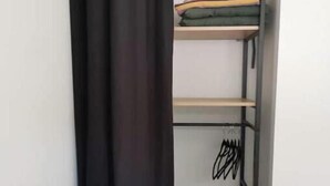 Una habitación con una cama, un armario metálico negro y una cortina.