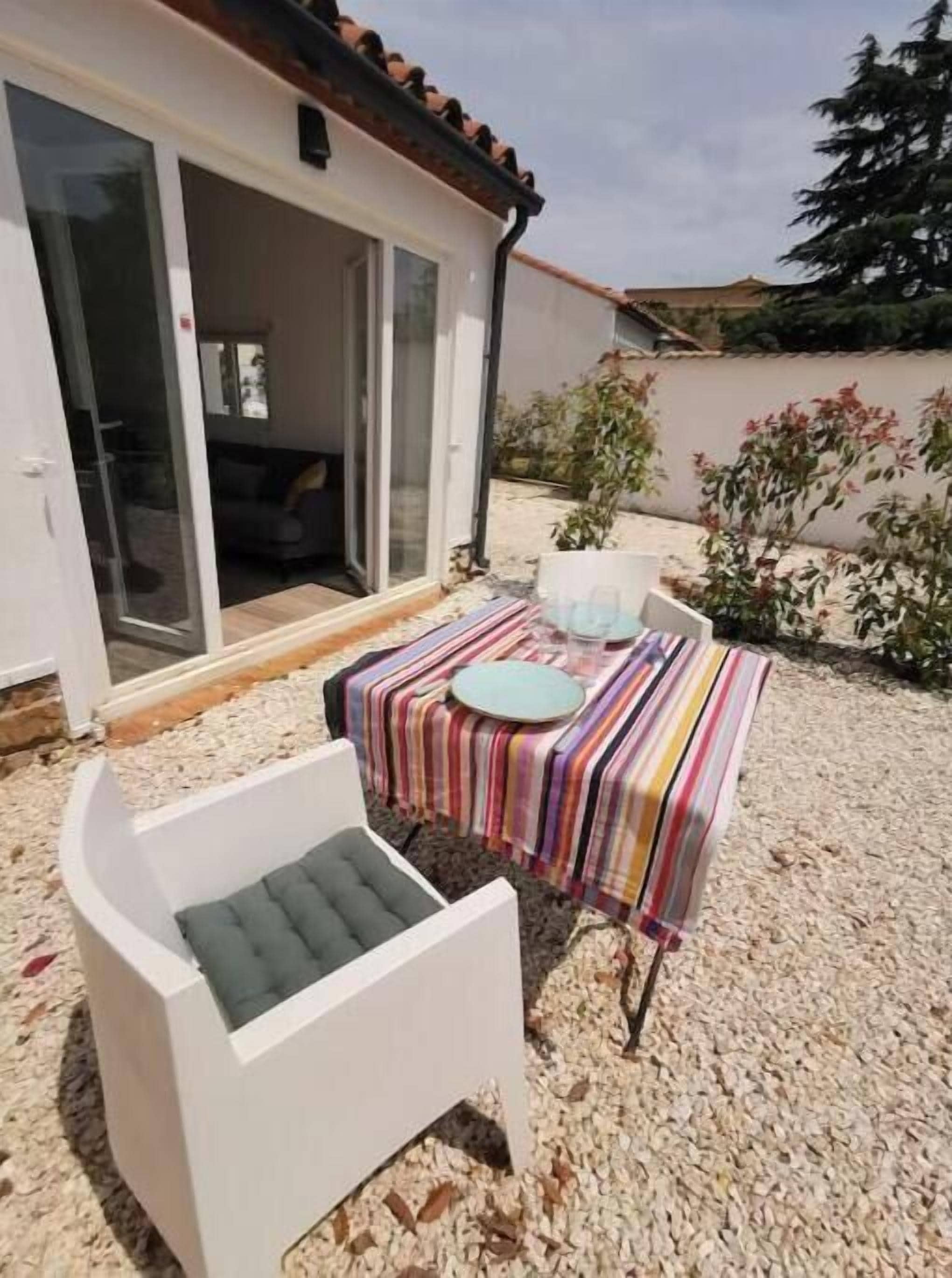 A patio with a striped tablecloth, a white chair, and a small table with a plate and a cup.