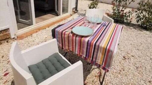 Un patio con mantel a rayas, una silla blanca y una mesa pequeña con un plato y una taza.