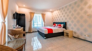 Habitación de hotel con cama, escritorio, silla, televisión y ventana con cortinas.