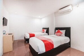 A hotel room with two beds, a desk, a TV, and an air conditioning unit.