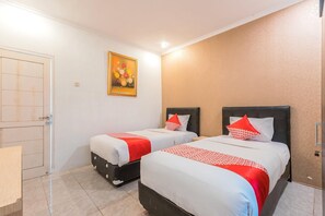 Una habitación de hotel con dos camas, una puerta, un cuadro y un papel tapiz estampado.