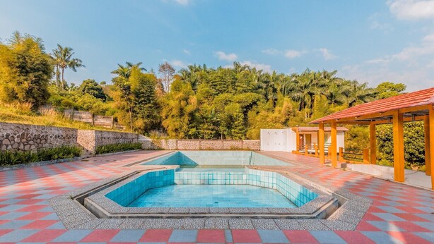 Una piscina con solárium de baldosas, rodeada de follaje y un muro de piedra.
