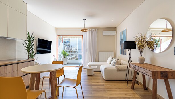 A modern living room with a sofa, a dining table with chairs, a wooden side table, and a large mirror. - Mandarin One Bedroom Apartment is a short walk from the beach & the town center (Vari)