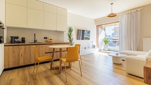 A modern kitchen with wooden cabinets, a dining table with yellow chairs, a round coffee table, and a sofa in a living area with a large window. - Mandarin One Bedroom Apartment is a short walk from the beach & the town center (Vari)