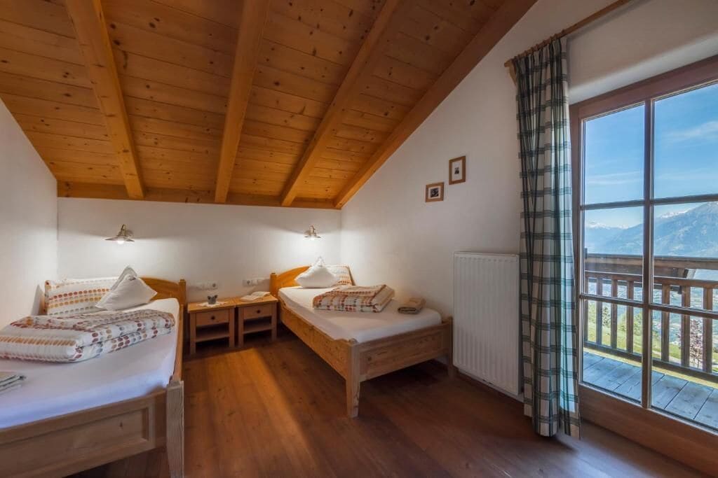 A room with two wooden beds, a wooden ceiling, a window with a view, and a radiator.