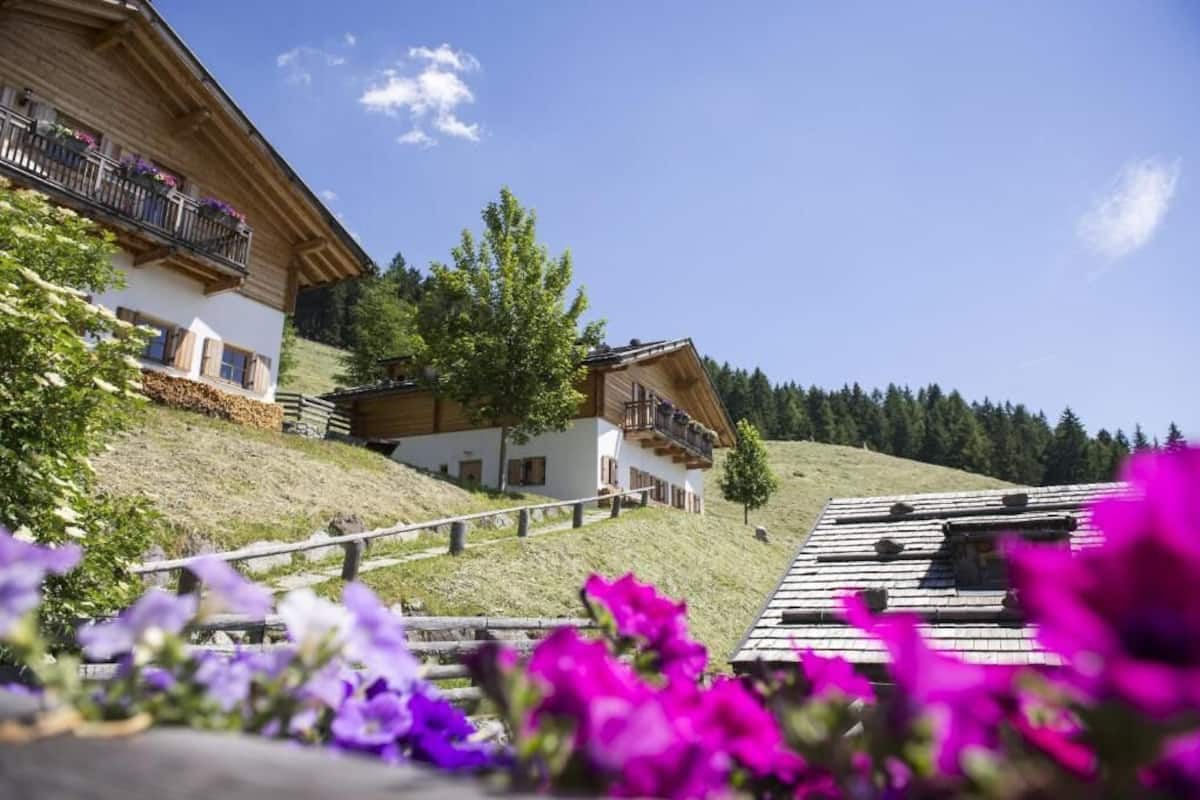 A traditional chalet with wooden balconies, a sloped roof, and a view of a forested hillside.