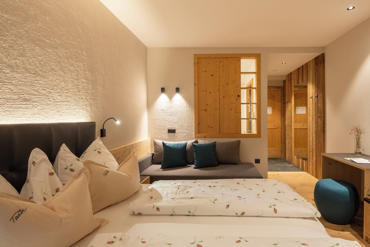 A modern hotel room with a bed, a desk, a TV, and a wooden wardrobe.