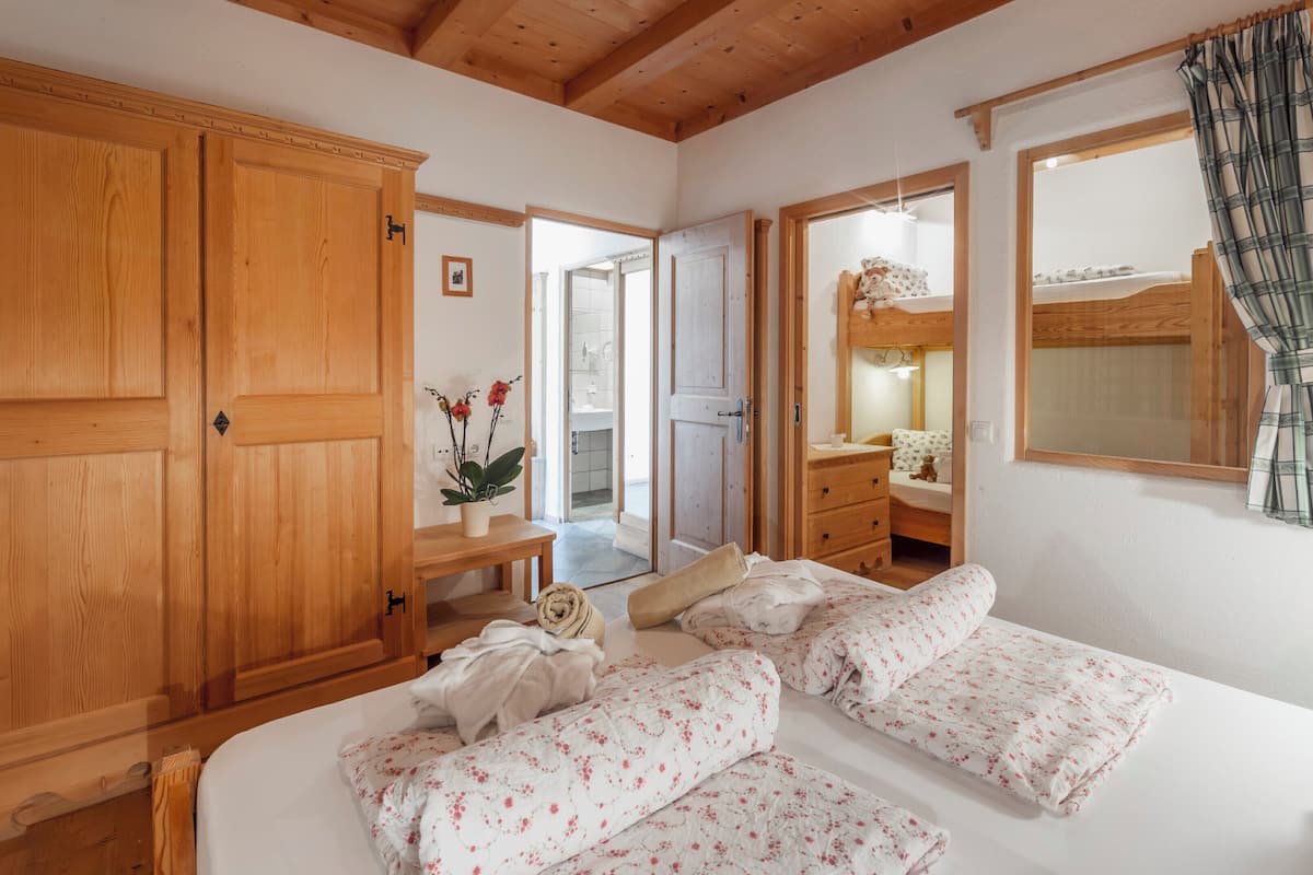 A bedroom with wooden furniture, a bed with floral bedding, a wooden wardrobe, and a mirror.