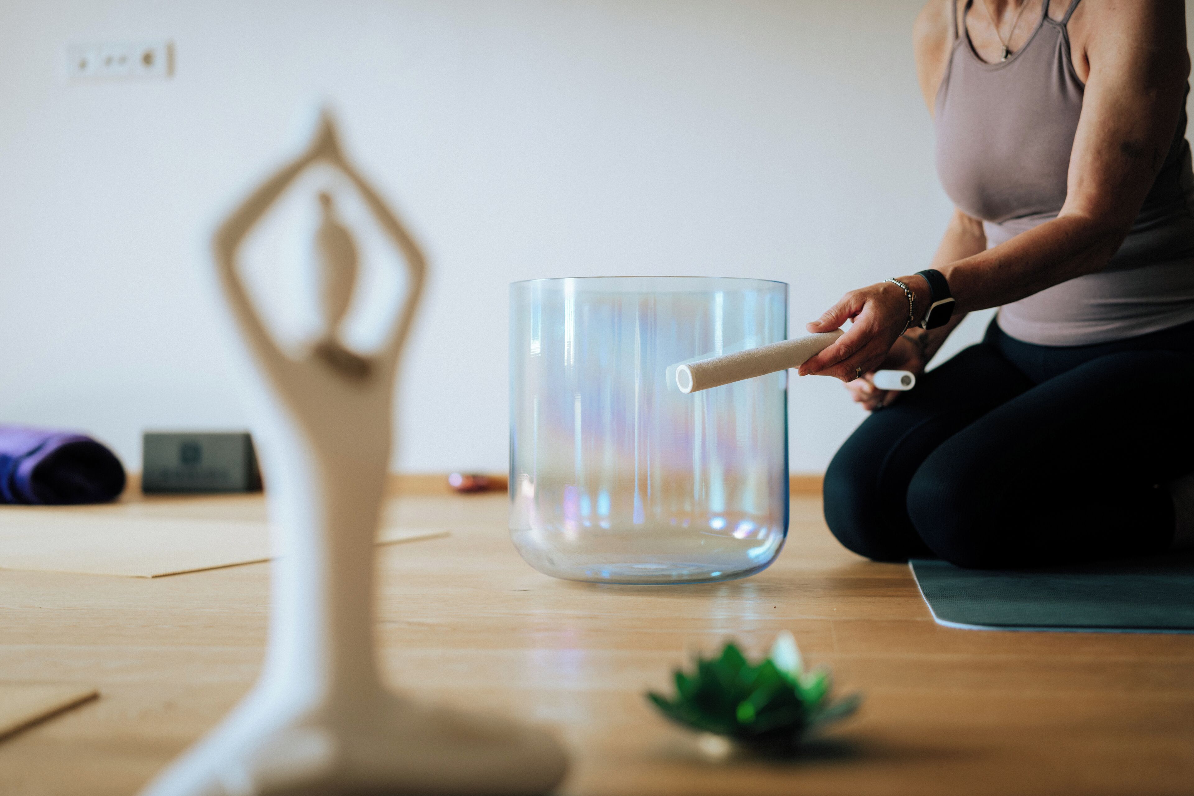 Una persona seduta su un tappetino da yoga, con un contenitore di vetro e un oggetto bianco su un pavimento di legno.