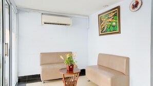A room with a beige sofa, a small wooden table with a potted plant, an air conditioning unit, and a framed picture on the wall.