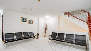 A waiting area with two rows of black chairs, a staircase with a red handrail, and two framed pictures on the wall.