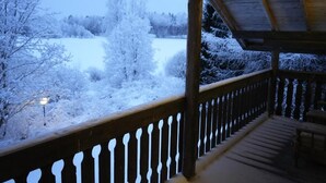 A wooden deck with a railing, overlooking a snowy landscape with trees and a path. - Old School Lodge Tahko Beach House (Kuopio)