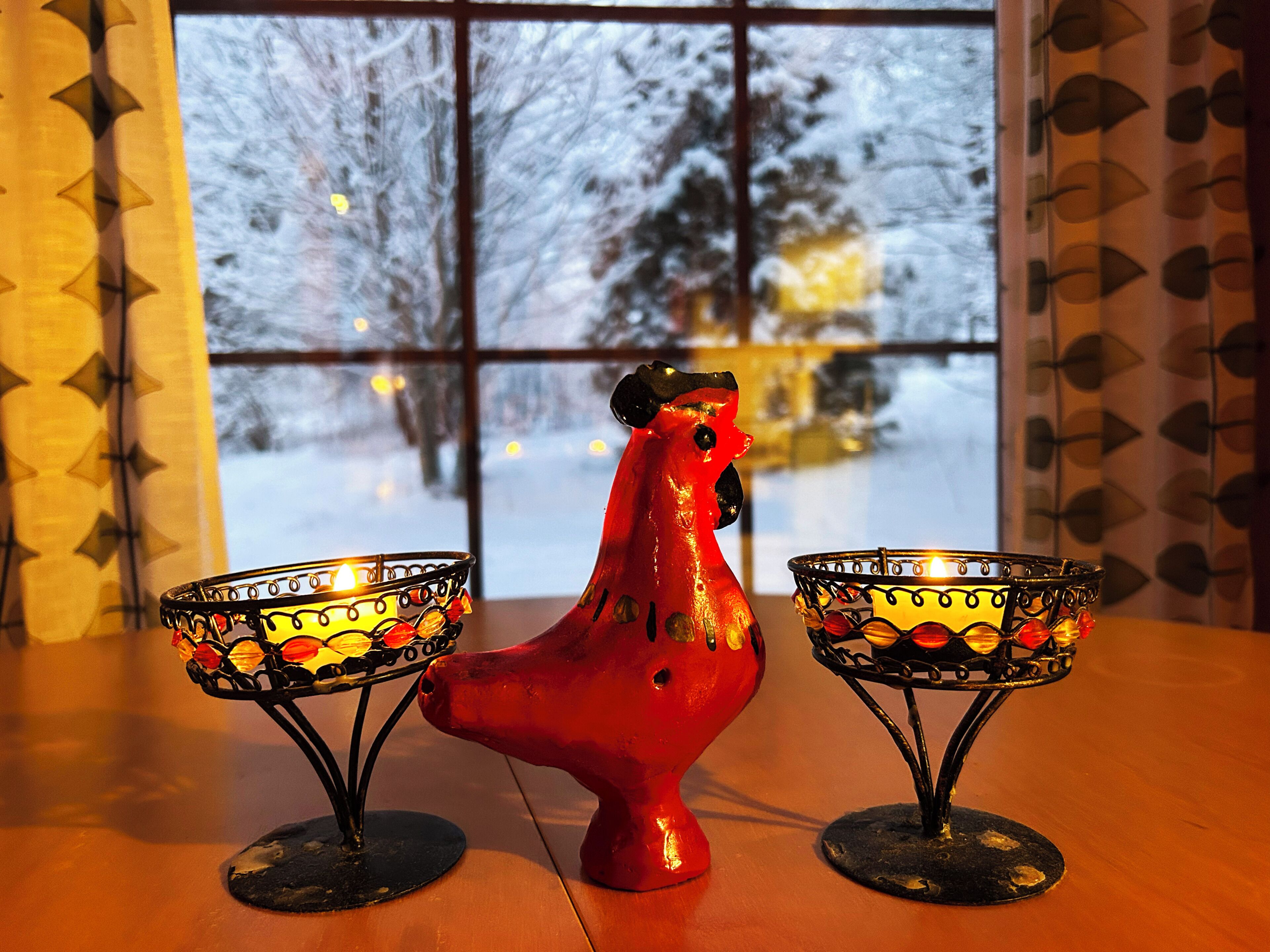A red ceramic rooster between two candle holders on a table.