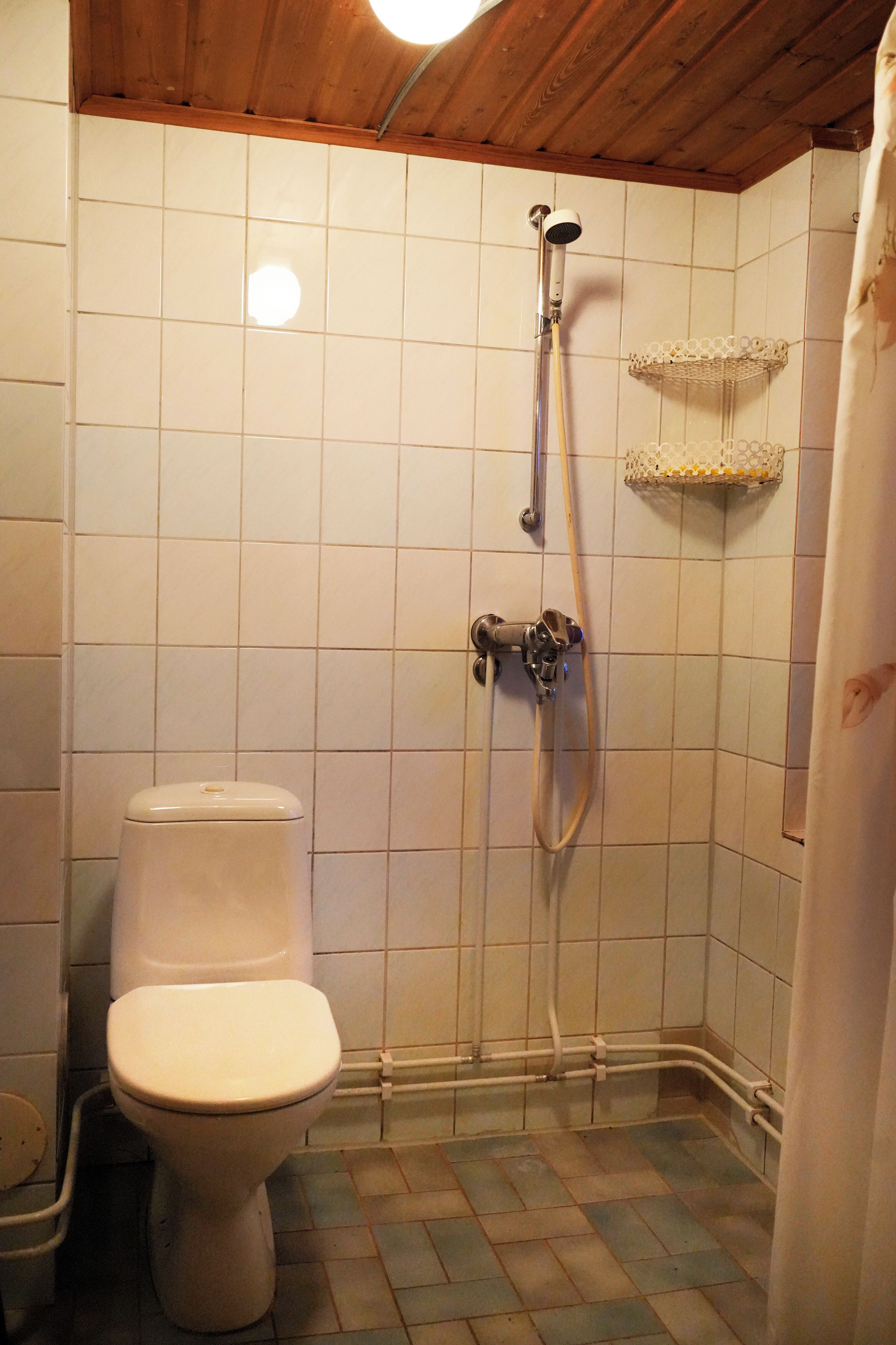 Un baño con inodoro, ducha y suelo de baldosas.