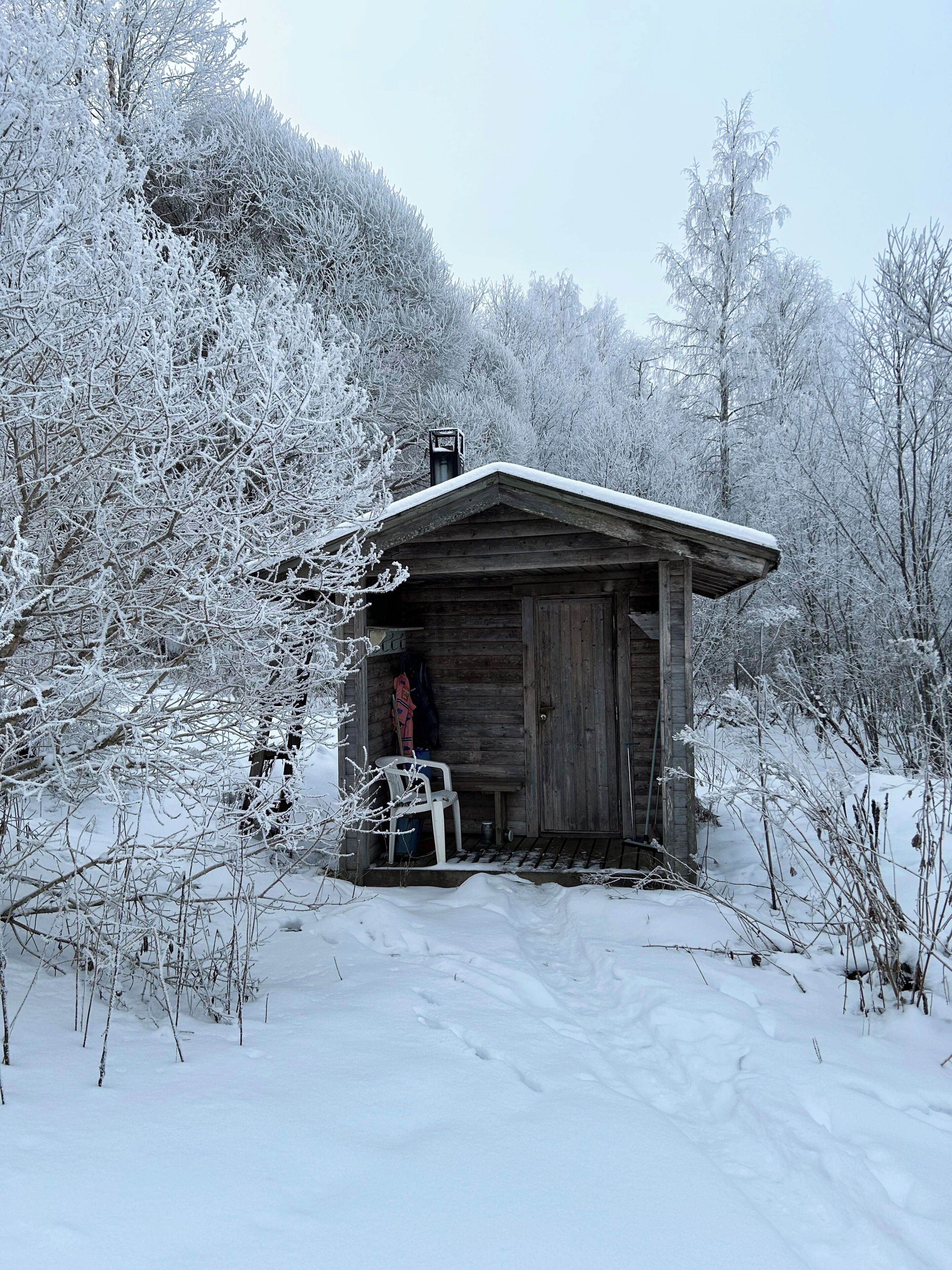 Una cabaña de madera con techo inclinado, rodeada de árboles cubiertos de nieve y un cielo despejado.