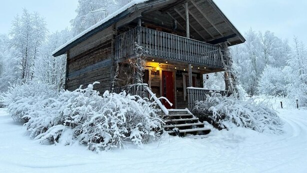 A wooden cabin with a balcony, surrounded by snow-covered trees. - Old School Lodge Tahko Beach House (Kuopio)