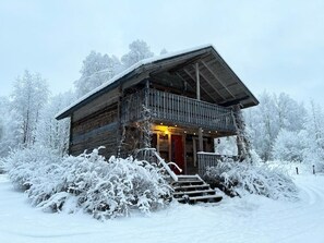 A wooden cabin with a balcony, surrounded by snow-covered trees. - Old School Lodge Tahko Beach House (Kuopio)
