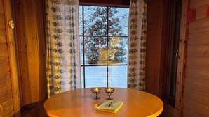 A wooden interior with a round table, two candles, and a window with a view of snow-covered trees. - Old School Lodge Tahko Beach House (Kuopio)