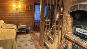 A cozy log cabin interior with a brick fireplace, wooden walls, a staircase, and a small table with chairs. - Old School Lodge Tahko Beach House (Kuopio)