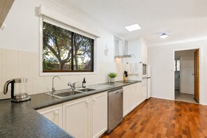 A modern kitchen with a dishwasher, double sink, and a window with a view of trees. - Escape Away by Ready Set Stay (Cowes)