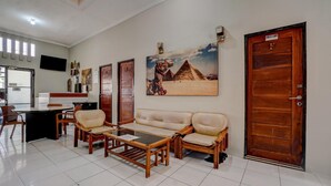 Ein Empfangsbereich mit einer Couch, Sesseln, einem Couchtisch, einem Schreibtisch und einem an der Wand montierten Fernseher.