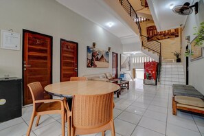 Un hall d’hôtel avec une table ronde en bois, des chaises en osier, un canapé, un escalier et un ventilateur fixé au mur.