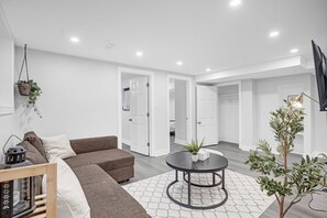 A modern living room with a sofa, a round table, and a hanging plant. - Cozy 2 Bedroom+50" TV+Sleeps 6+Lower Unit (Kitchener)