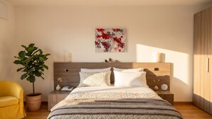 Ein Schlafzimmer mit einem Bett, einem Nachttisch, einer Topfpflanze, einem gelben Sessel und einem Holzschrank.