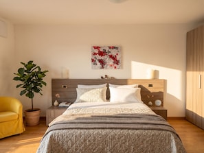 A bedroom with a bed, a nightstand, a potted plant, a yellow chair, and a wooden wardrobe. - Voiandes balcony apartment garden and pool (Tremosine)