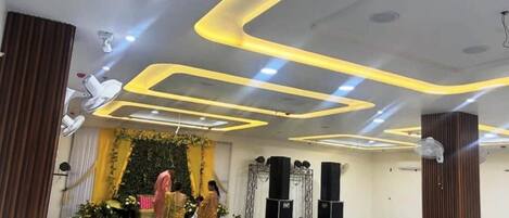 A conference room with modern lighting, a stage with speakers, and rows of seating.