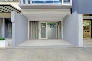 Ein modernes Gebäudeeingang mit Glastür, einem kleinen Balkon und einem Betonfußboden.